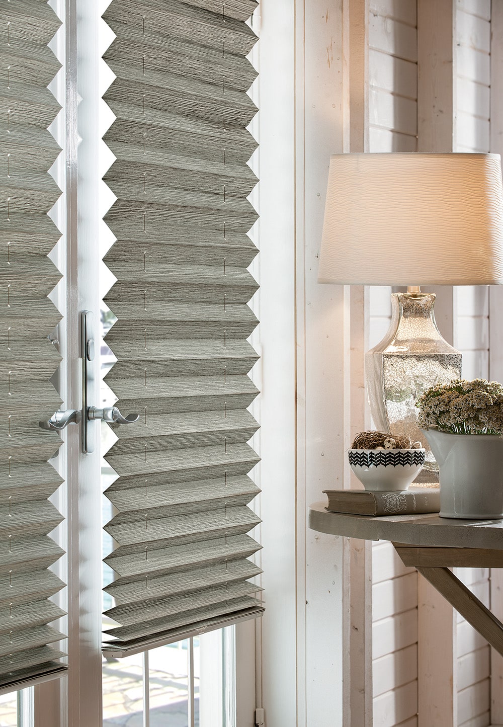 Close-up of pleated shades in a living room with a lamp on a table beside them.