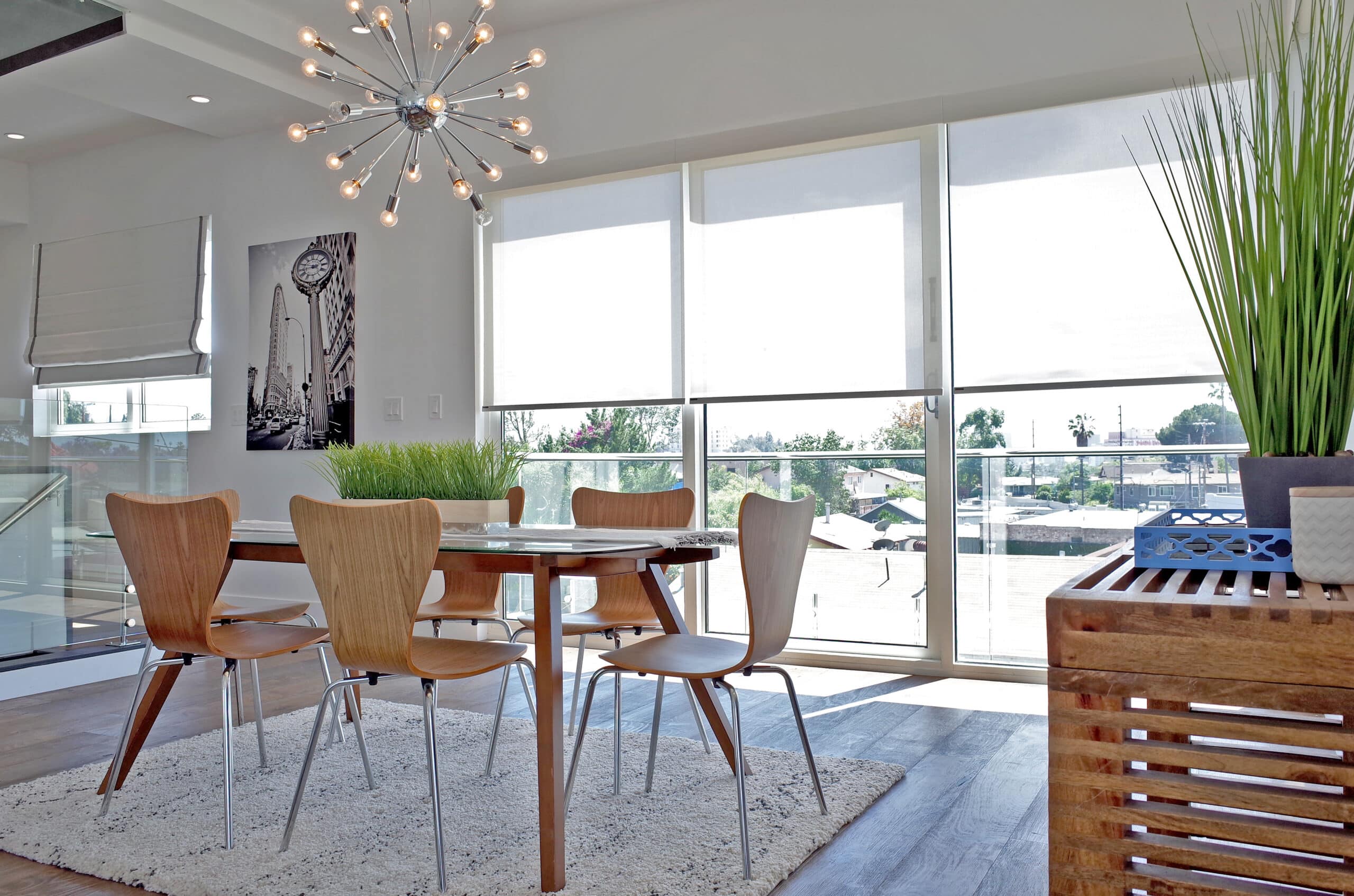 Roller shades halfway opened, filtering in light into a simplistic dining room. 