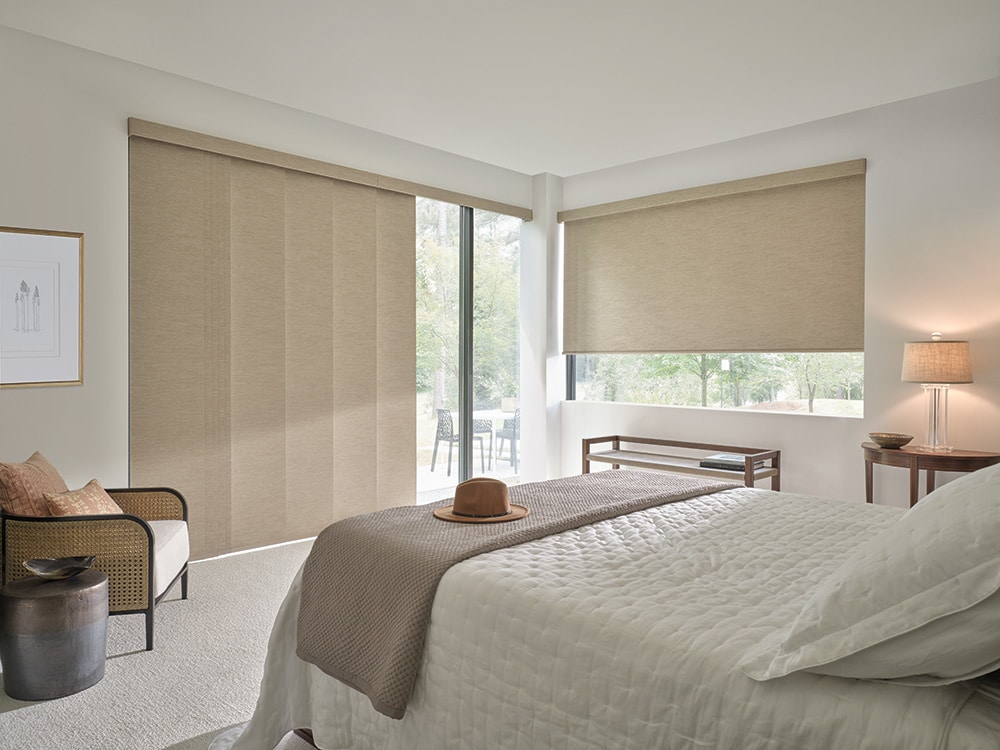 A blackout roller shade and a blackout vertiglide shade both partly covering the window blocking out light in a master bedroom. 